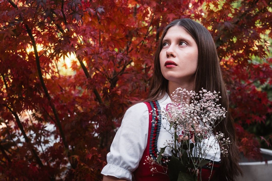 En kvinna i en traditionell dirndl framför röda höstlöv.