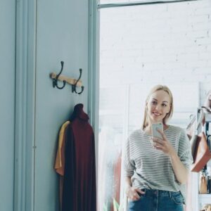 Kvinna fotograferar sig själv i spegeln med mobilen bland kläder